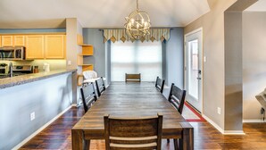 A spacious dining area with a long wooden table, surrounded by chairs, and a kitchen area with wooden cabinets and a microwave. - Swim, Game, Relax & More: Family Getaway in Frisco (Frisco)