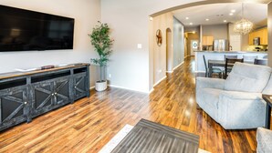 A spacious living room with a large flat-screen TV, wooden flooring, and a grey armchair. - Swim, Game, Relax & More: Family Getaway in Frisco (Frisco)