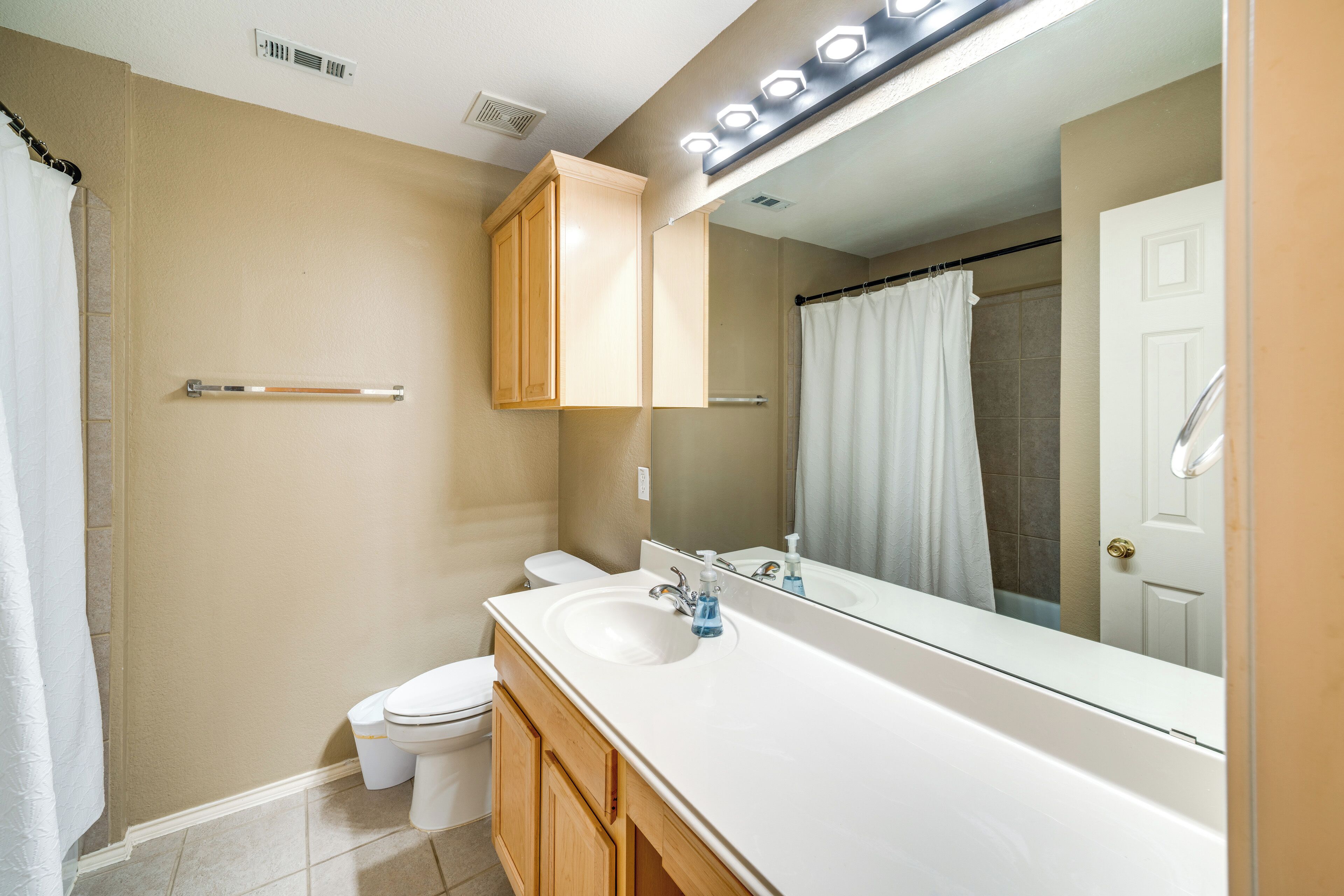 A bathroom with a white sink, mirror, and toilet. There is a shower curtain and a towel rack.