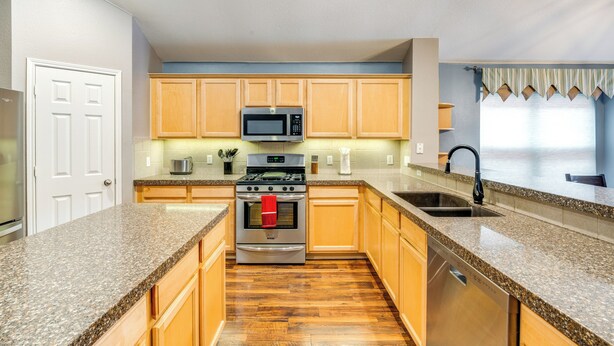 A kitchen with granite countertops, wooden cabinets, stainless steel appliances, and a dishwasher. - Swim, Game, Relax & More: Family Getaway in Frisco (Frisco)