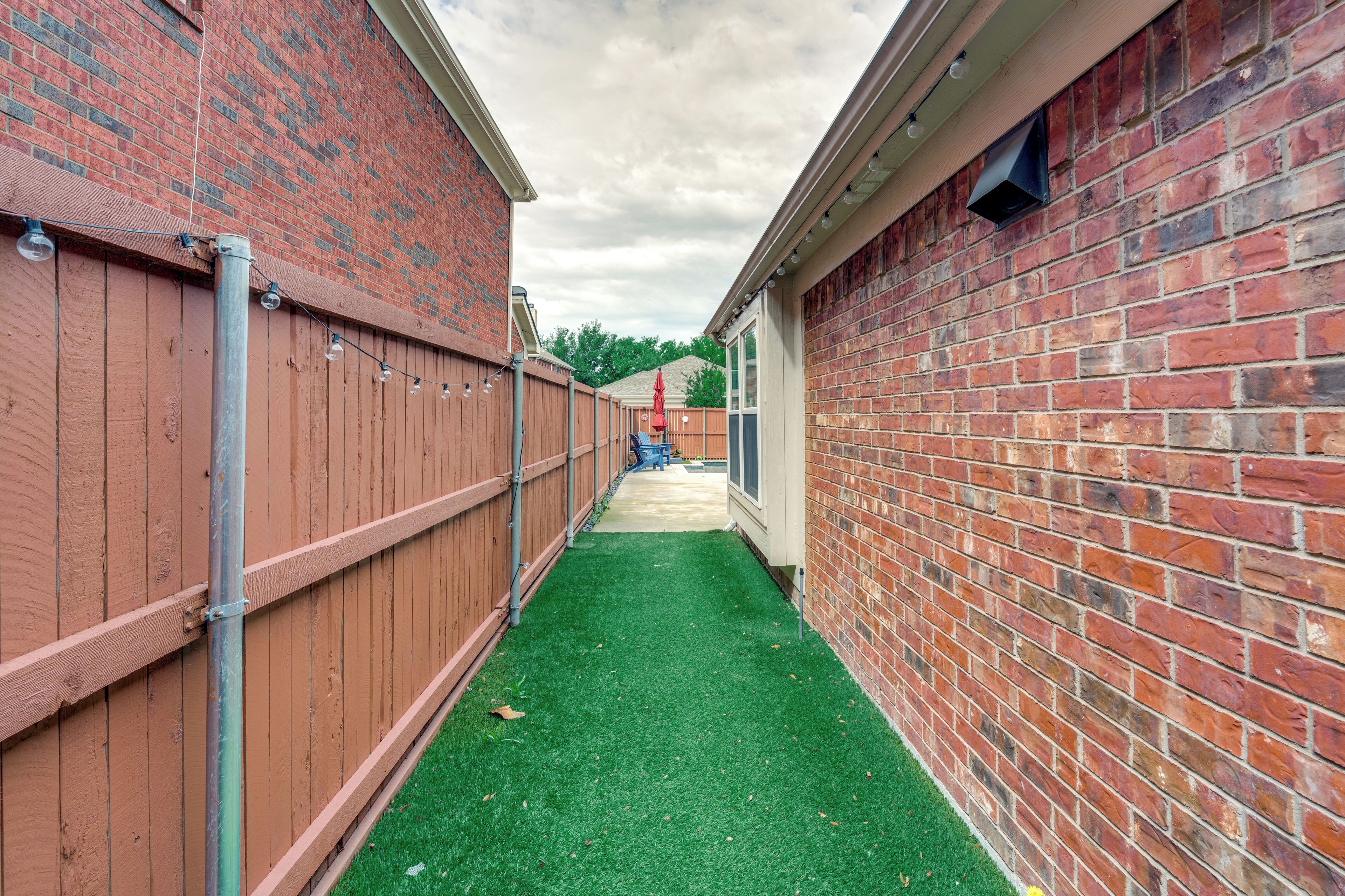 A narrow pathway flanked by brick walls, leading to a building with a visible door and windows.