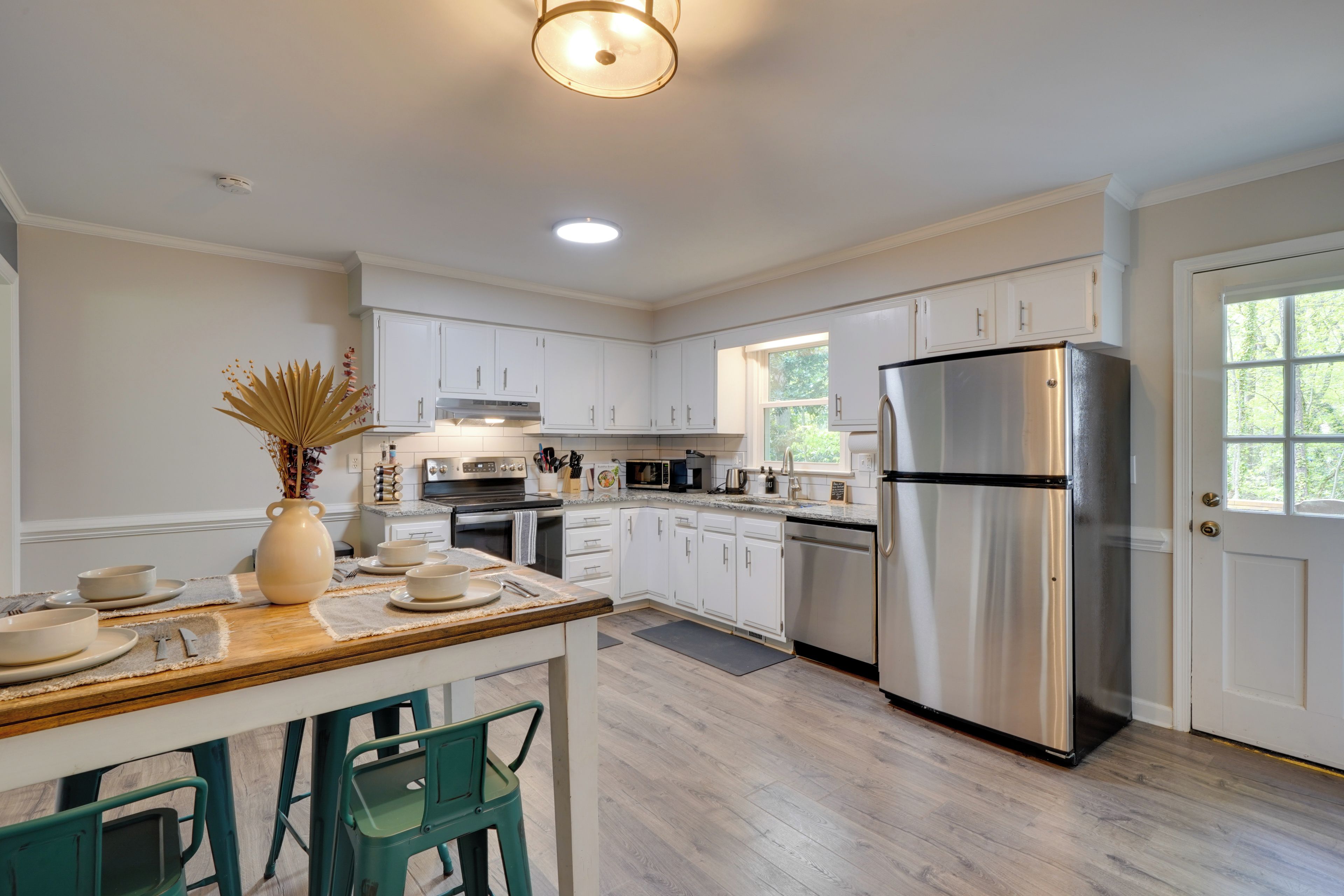 A modern kitchen with white cabinets, a stainless steel refrigerator, and a dining area with a wooden table and chairs.