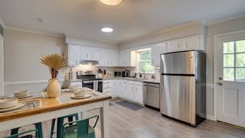 A modern kitchen with white cabinets, a stainless steel refrigerator, and a dining area with a wooden table and chairs.