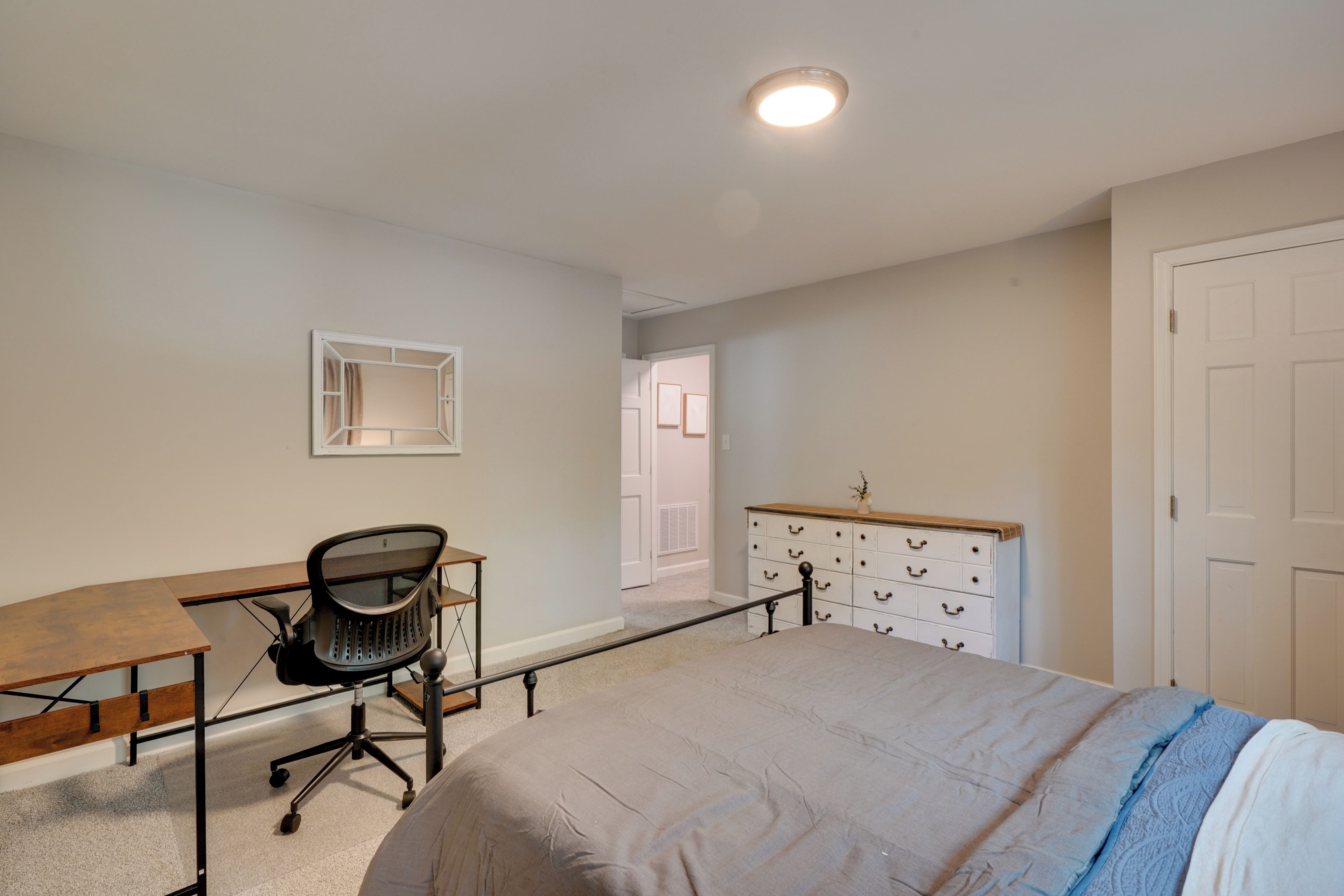 A bedroom with a bed, a desk, a chair, a dresser, and a door.