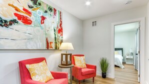 A modern living room with two red armchairs, a small round table with a lamp, and a colorful abstract painting on the wall. - 3 Mi to Dtwn Entertainment: Pensacola Family Home! (Pensacola)