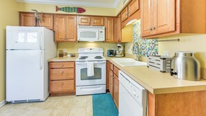 A kitchen with wooden cabinets, a white refrigerator, a microwave, an oven, a sink, and a coffee maker.