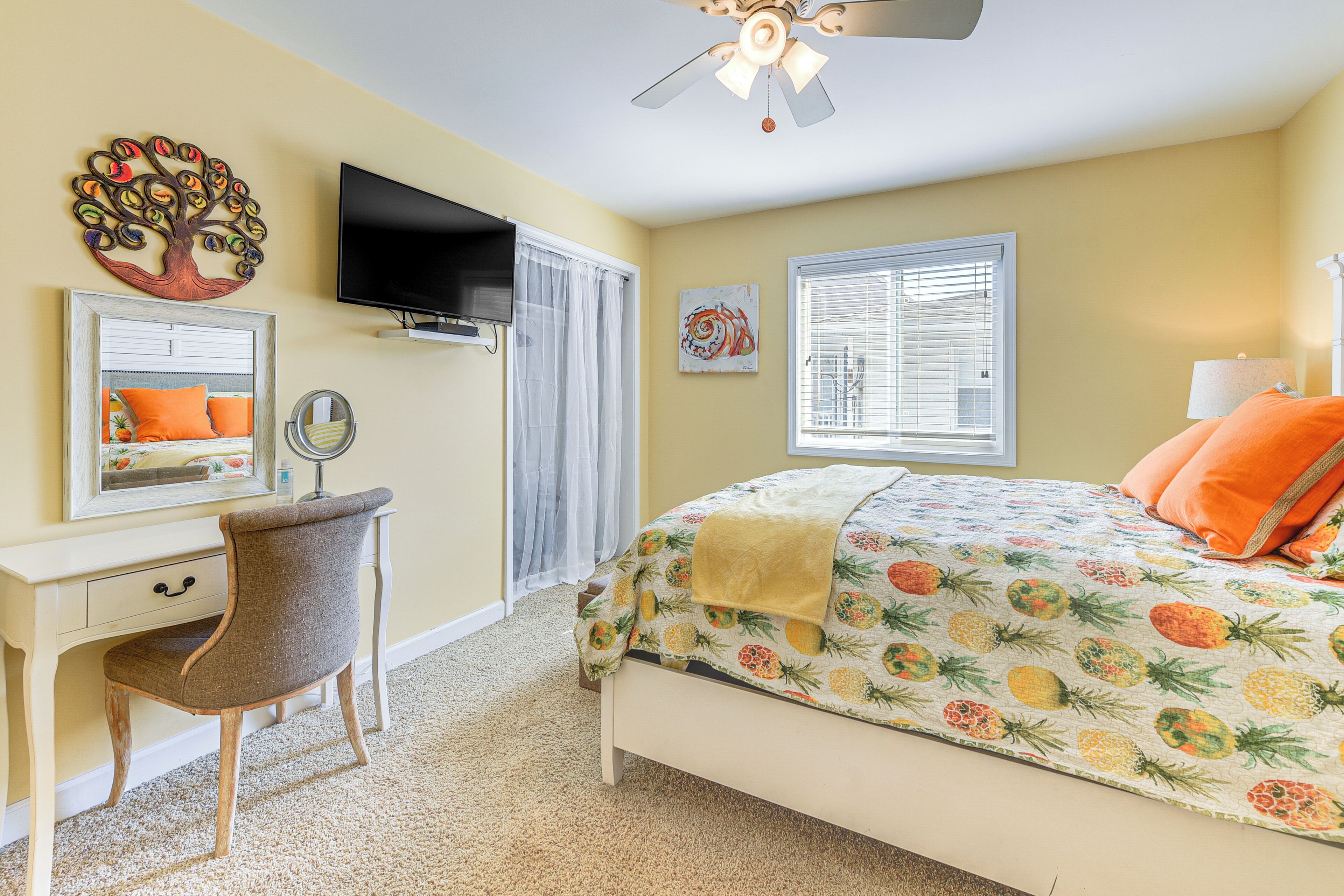 A bedroom with a bed, a desk with a chair, a television, and a ceiling fan.