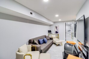 A modern living room with a sofa, armchairs, a flat-screen TV, and a gaming console. - Newly Renovated Abode w/ Patio in Baltimore! (Baltimore)