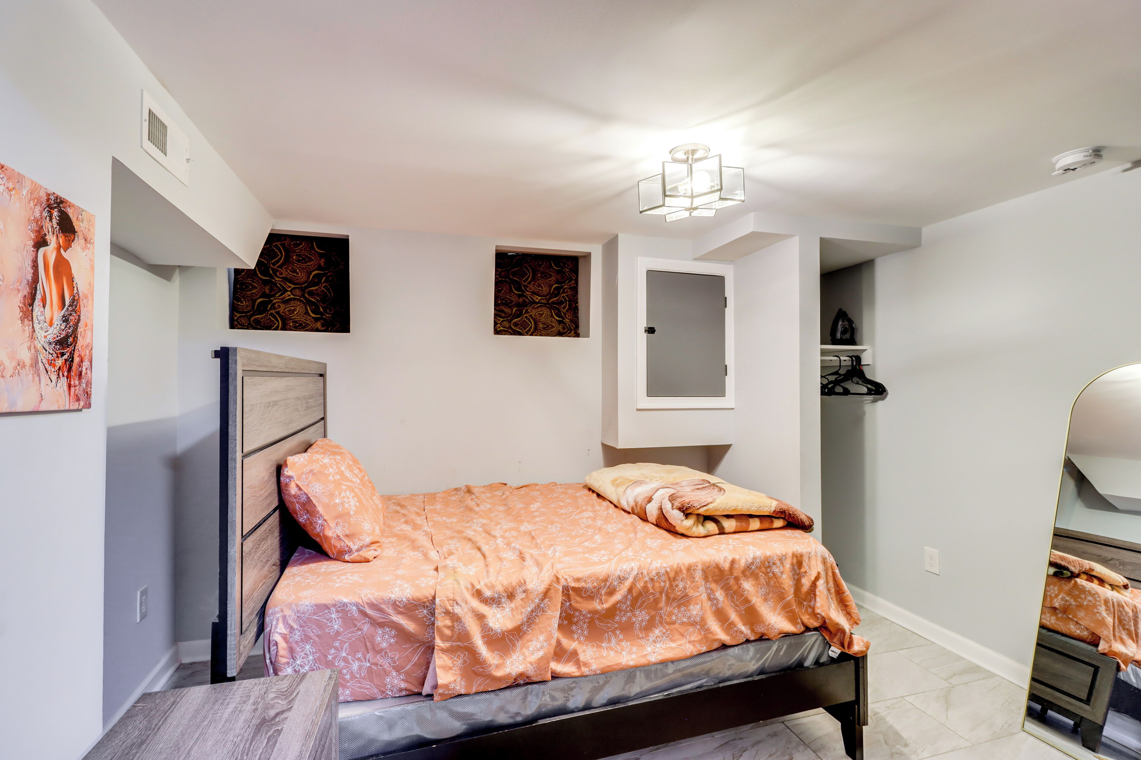 A bedroom with a bed, a bedside table, a mirror, and artwork on the walls.