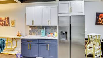 A modern kitchen with white and dark blue cabinets, a stainless steel refrigerator, and a marble backsplash.