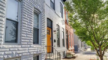 A row of townhouses with a brick facade, a yellow door, and a tree in the foreground.