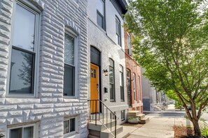A row of townhouses with a brick facade, a yellow door, and a tree in the foreground. - Newly Renovated Abode w/ Patio in Baltimore! (Baltimore)