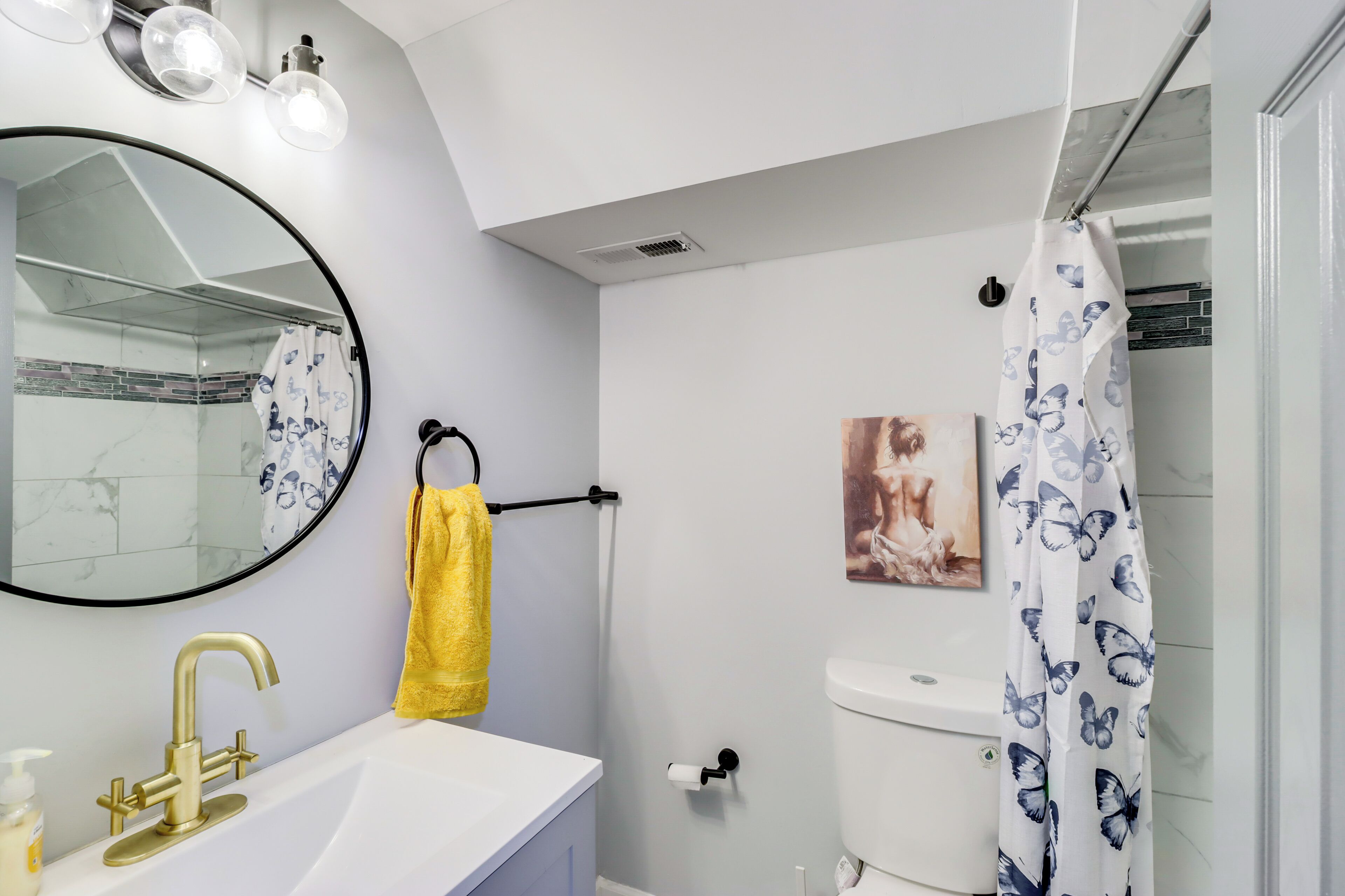 A bathroom with a white sink, gold faucet, and a yellow towel.