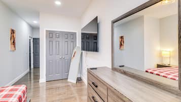 A bedroom with a bed, dresser, mirror, and a door leading to another room.
