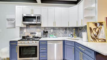 A modern kitchen with white and blue cabinets, stainless steel appliances, and marble backsplash.