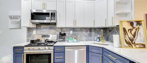 Una cocina moderna con gabinetes blancos y azules, electrodomésticos de acero inoxidable y una salpicadera de mármol.