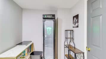 A compact room with a white door, a small table with a box, a trash bin, and a tall appliance with a green logo.