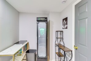Una stanza piccola con una porta bianca, un tavolino con una scatola, un cestino e un elettrodomestico alto con un logo verde.