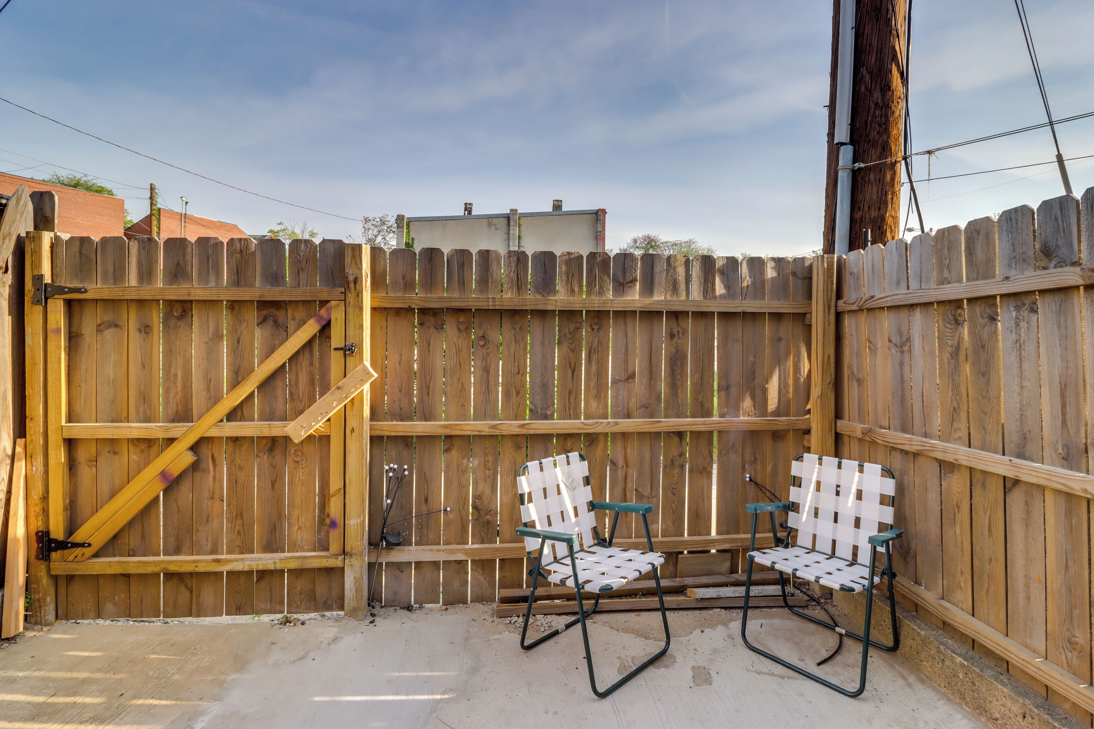 A wooden fence with a gate, two chairs with checkered patterns, and a concrete ground.