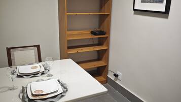 Un comedor con una mesa blanca preparada para dos, una estantería de madera y un cuadro en la pared.