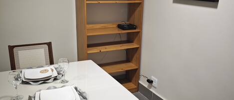 A dining area with a white table set for two, a wooden bookshelf, and a framed picture on the wall.