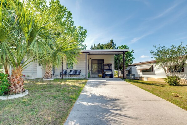 A single-story house with a covered porch, a driveway, and a lawn with palm trees.