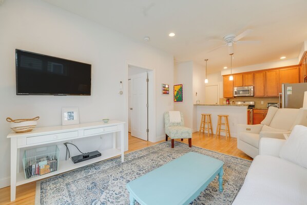 A modern living room with a flat-screen TV, a light blue coffee table, and a white sofa.
