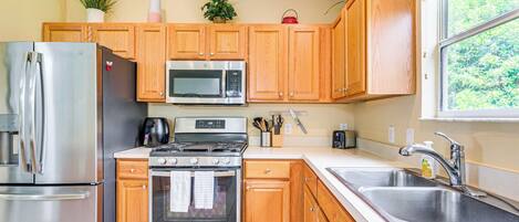 A kitchen with wooden cabinets, stainless steel appliances, and a window with a view of greenery.