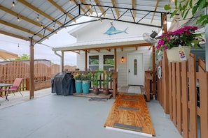 Uma área de varanda coberta com deck de madeira, mobiliário externo e vasos de plantas.