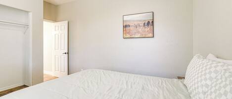 A bedroom with a bed, a door, and a wall-mounted picture.