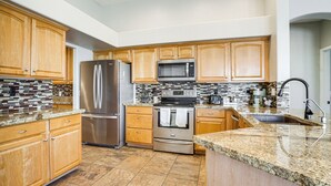 A modern kitchen with wooden cabinets, stainless steel appliances, and a granite countertop. - Private Pool + Patio: Desert Abode in Goodyear (Goodyear)