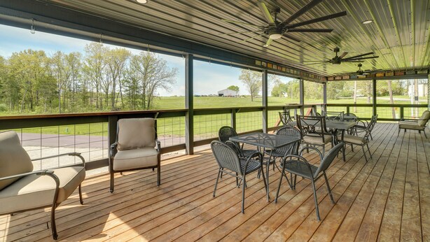 Une terrasse extérieure couverte, dotée d’un plancher en bois, de chaises et de tables en métal, ainsi que de ventilateurs de plafond.