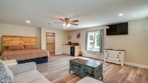 Une chambre à coucher comprenant un lit, un ventilateur de plafond, une commode, un téléviseur et une fenêtre avec des rideaux.