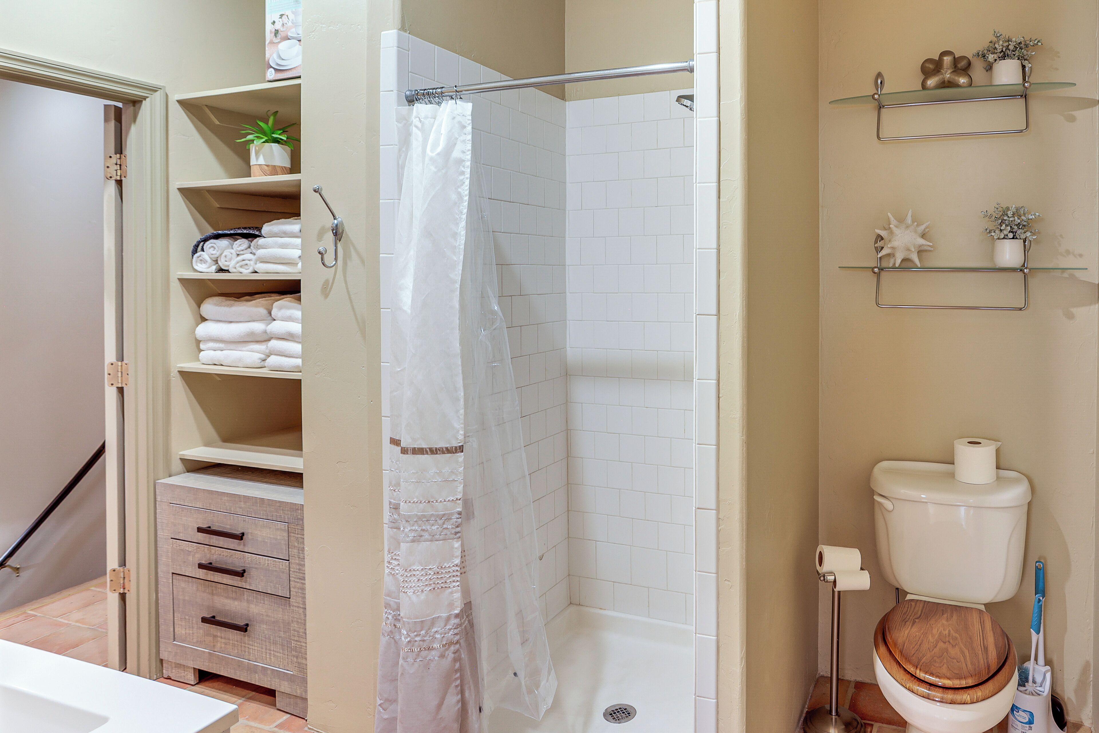 A bathroom with a shower, toilet, and storage shelves.