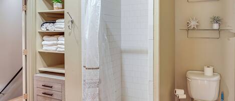 A bathroom with a shower, toilet, and storage shelves.