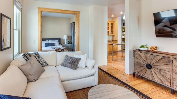 Una sala de estar con un sofá blanco, un mueble de madera y un televisor montado en la pared.