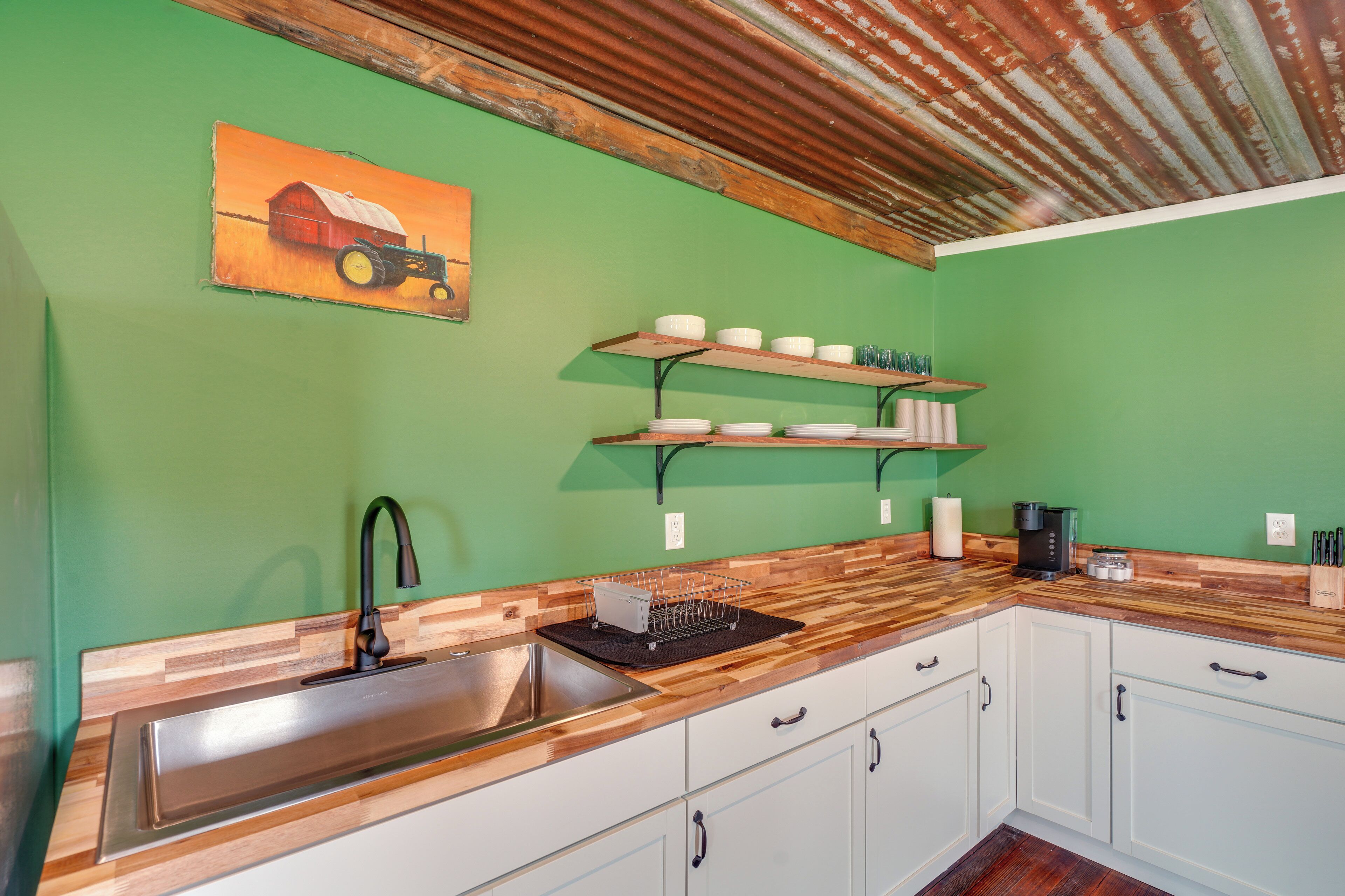 A kitchen with a wooden countertop, white cabinets, a stainless steel sink, and a coffee maker.
