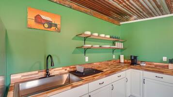 A kitchen with a wooden countertop, white cabinets, a stainless steel sink, and a coffee maker.