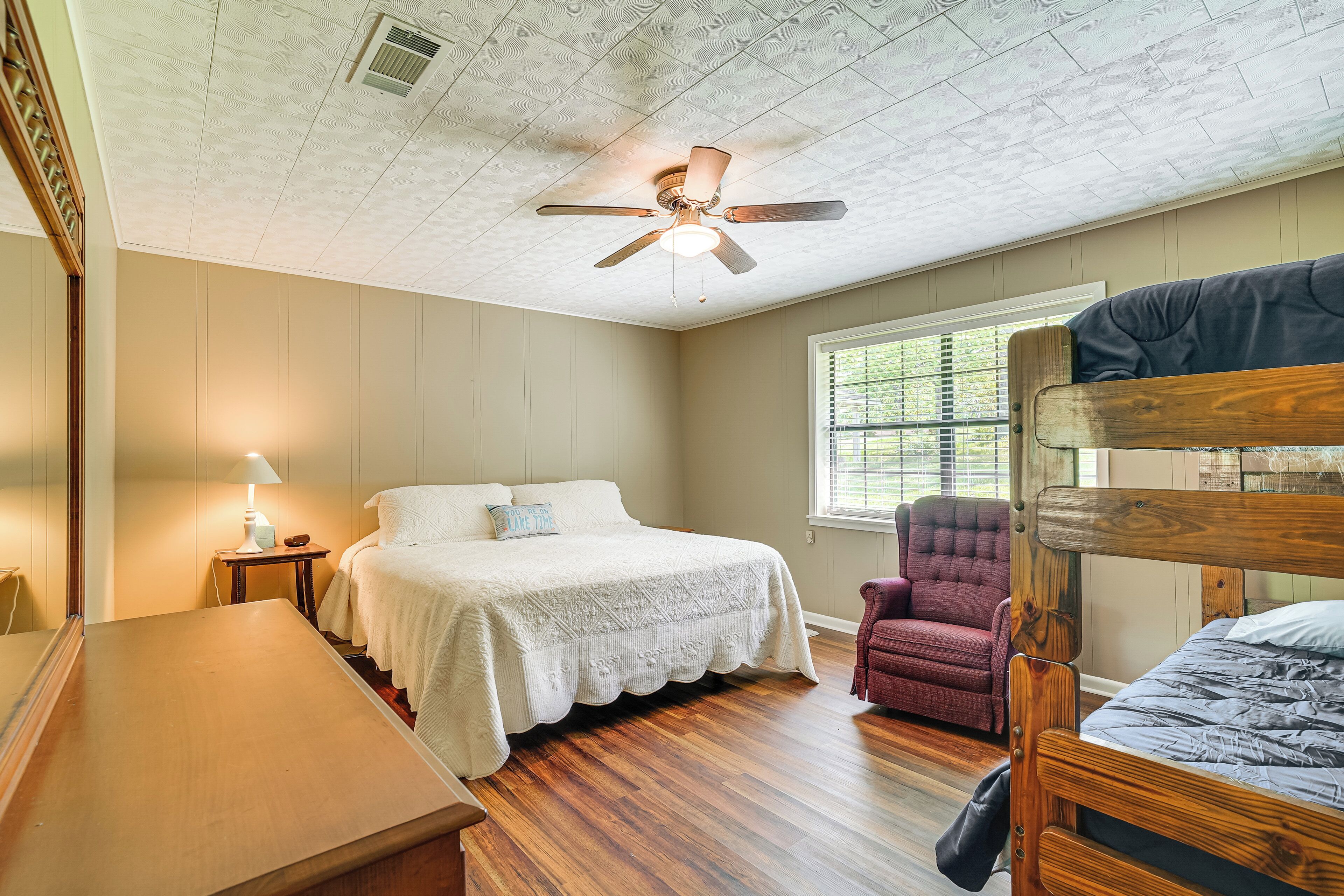 A bedroom with a wooden bed, a ceiling fan, a window with blinds, a chair, and a desk.
