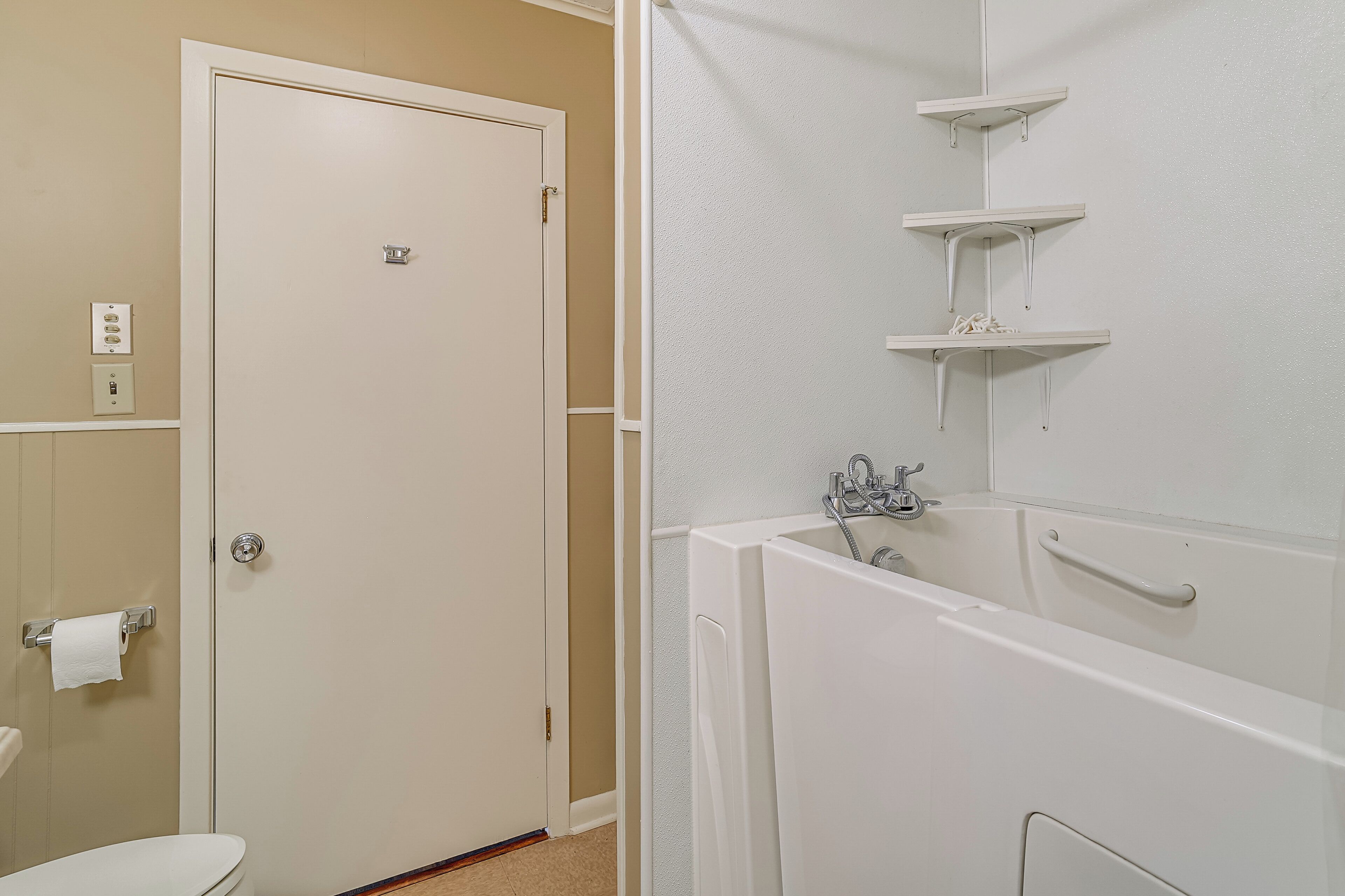 A bathroom with a toilet, sink, and bathtub. There are white shelves above the bathtub.
