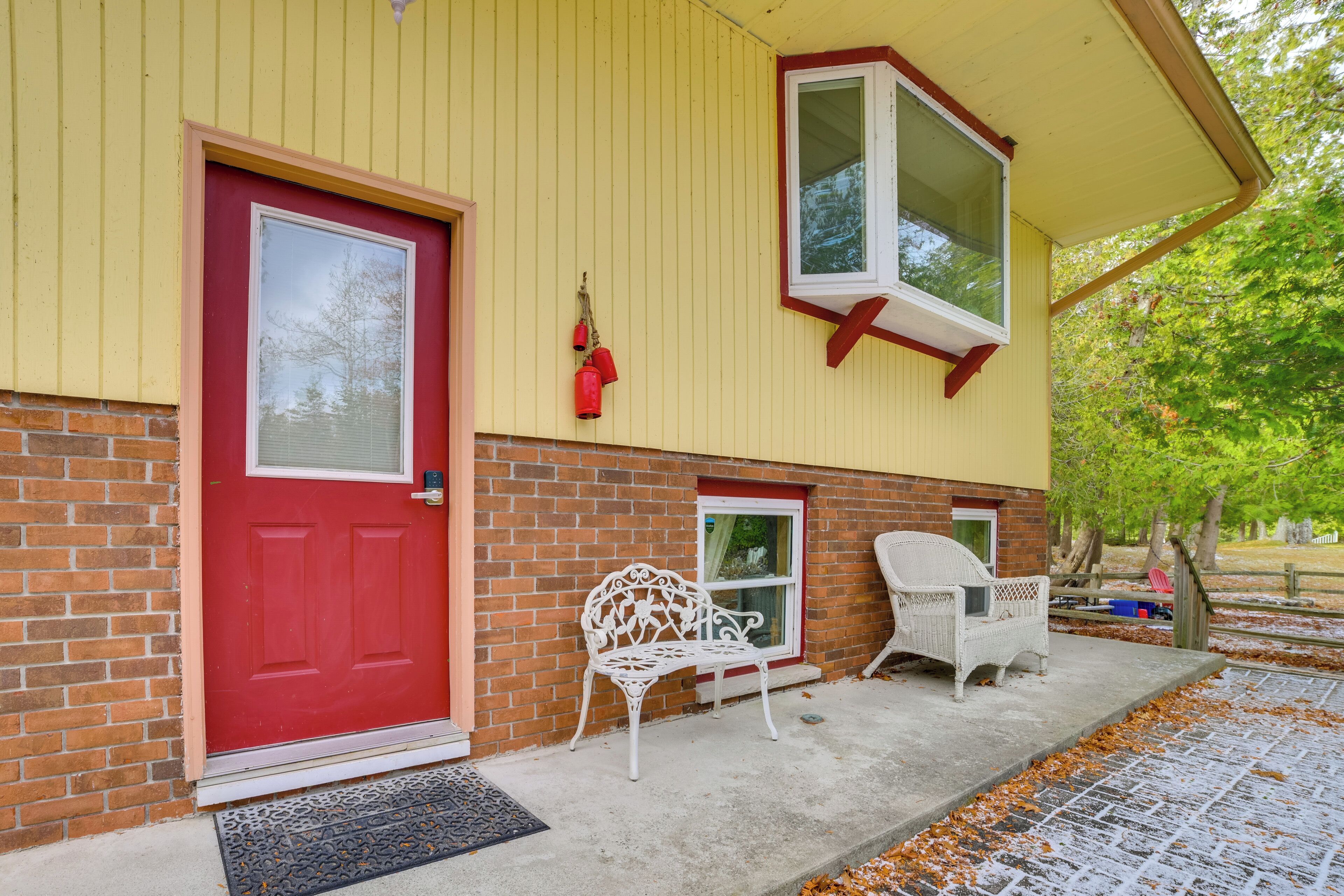 A yellow building with a red door, a white bench, and a white chair outside.