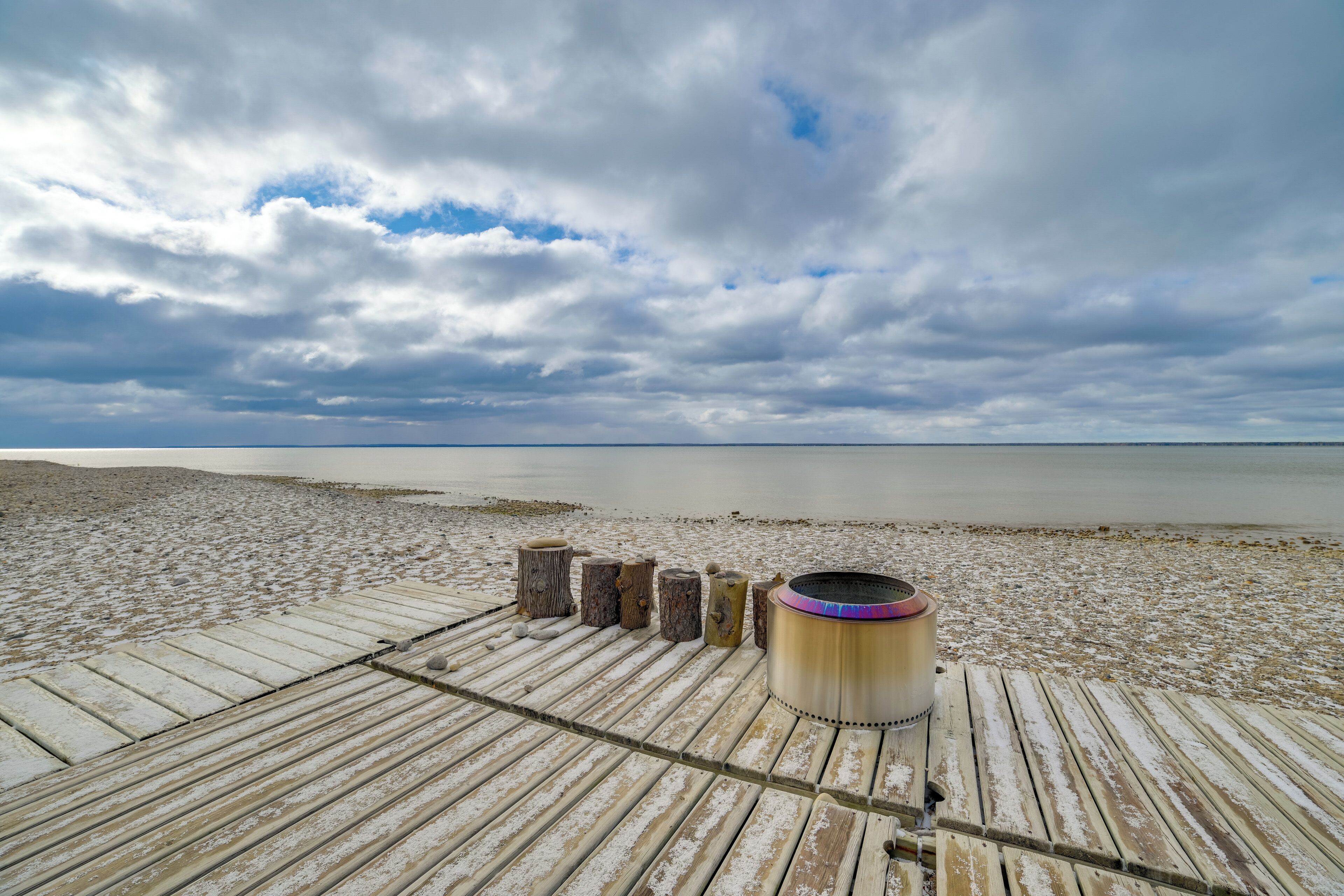 Een houten steiger die zich uitstrekt over een rustig wateroppervlak, met een metalen vat en houten palen langs de rand.