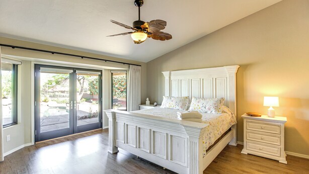 A bedroom with a large bed, a ceiling fan, a nightstand, and a sliding glass door leading to an outdoor area. - Newly Renovated Home w/ Pool Access in Tucson! (Saddlebrooke)