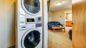 Un lavadero con lavadora y secadora apiladas, un reloj en la pared, y una sala de estar con sofá y mesa de centro.