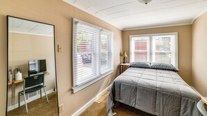 Un dormitorio con una cama, un escritorio con silla, una lámpara y dos ventanas con persianas.