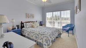 Un dormitorio con cama, mesita de noche, silla, ventilador de techo y ventana con persianas.