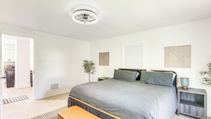A bedroom with a large bed, bedside tables, a bench, a ceiling fan, and a door leading to a bathroom.