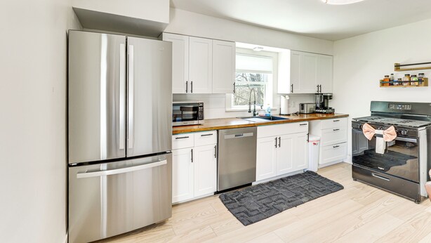 A modern kitchen with stainless steel appliances, white cabinetry, and a black rug.