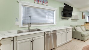 Una cocina con armarios blancos, lavavajillas de acero inoxidable y una ventana con persianas.