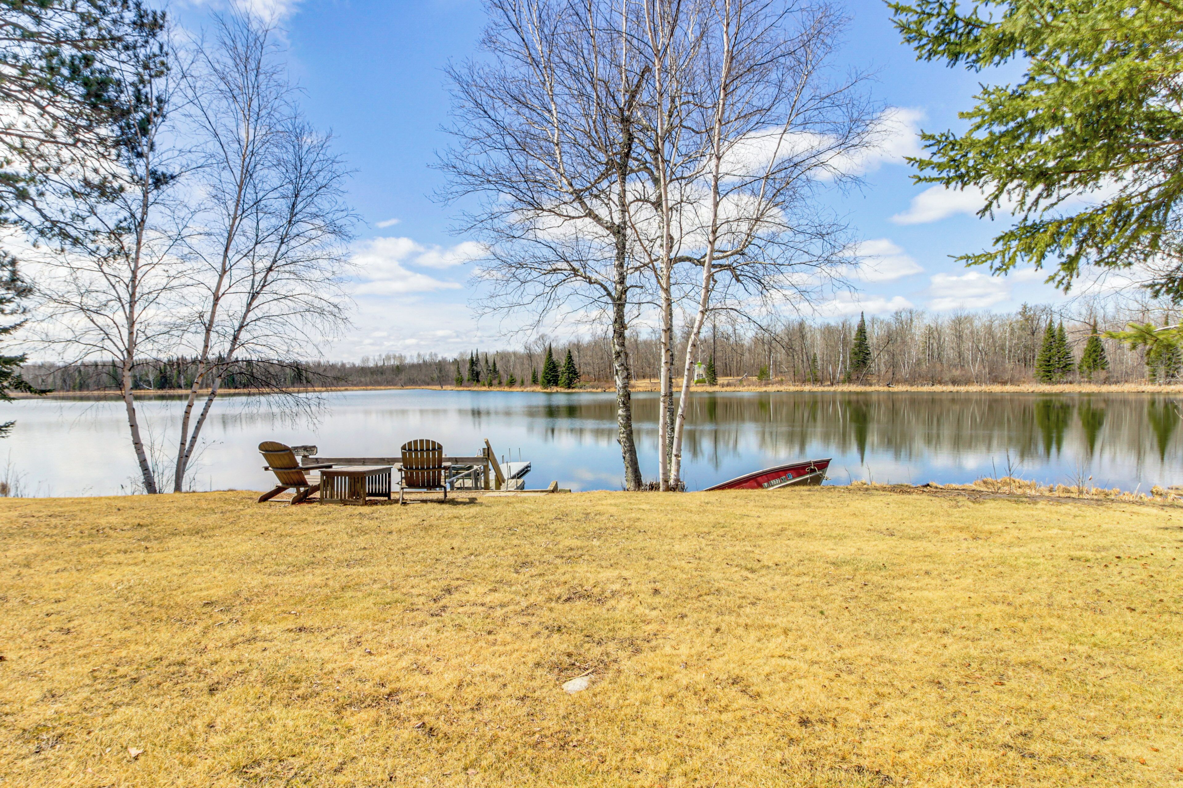 A lakeside setting with a table and chairs, a boat, and trees.